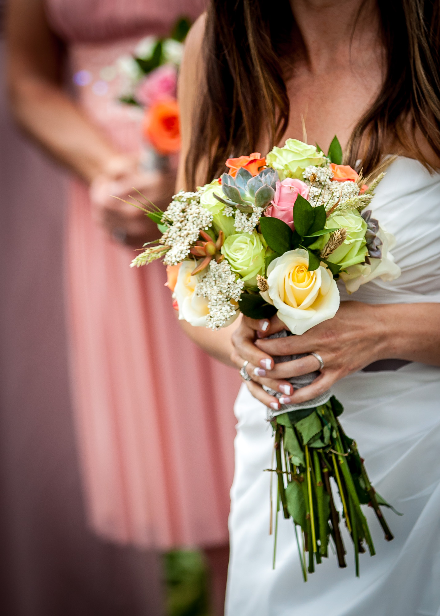 Bride holding a colorful wedding bouquet with bridesmaid in the background, highlighting the floral details and wedding theme.