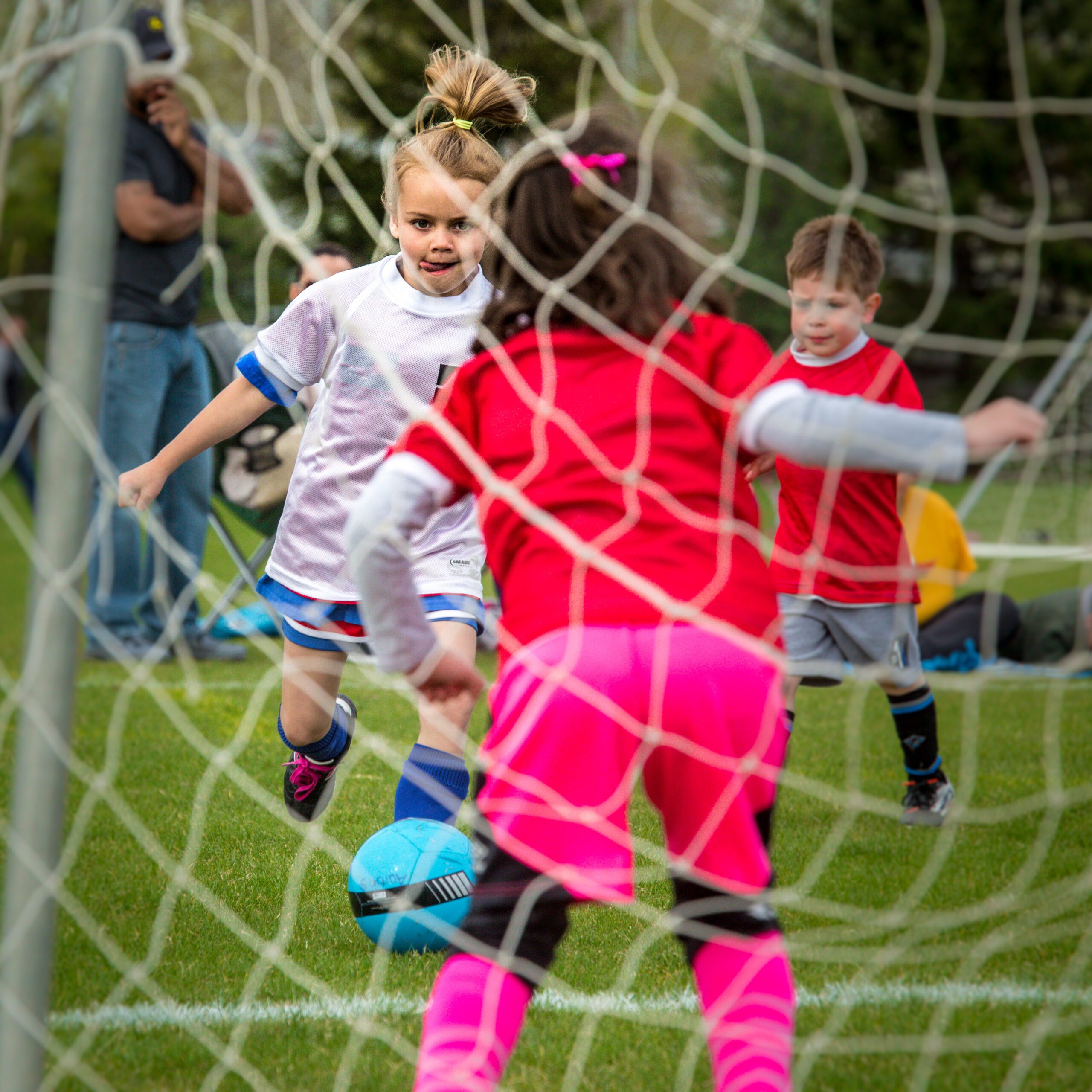 Young Girl in White Playing Soccer With Determination, With Teammates and Spectators in the Background.