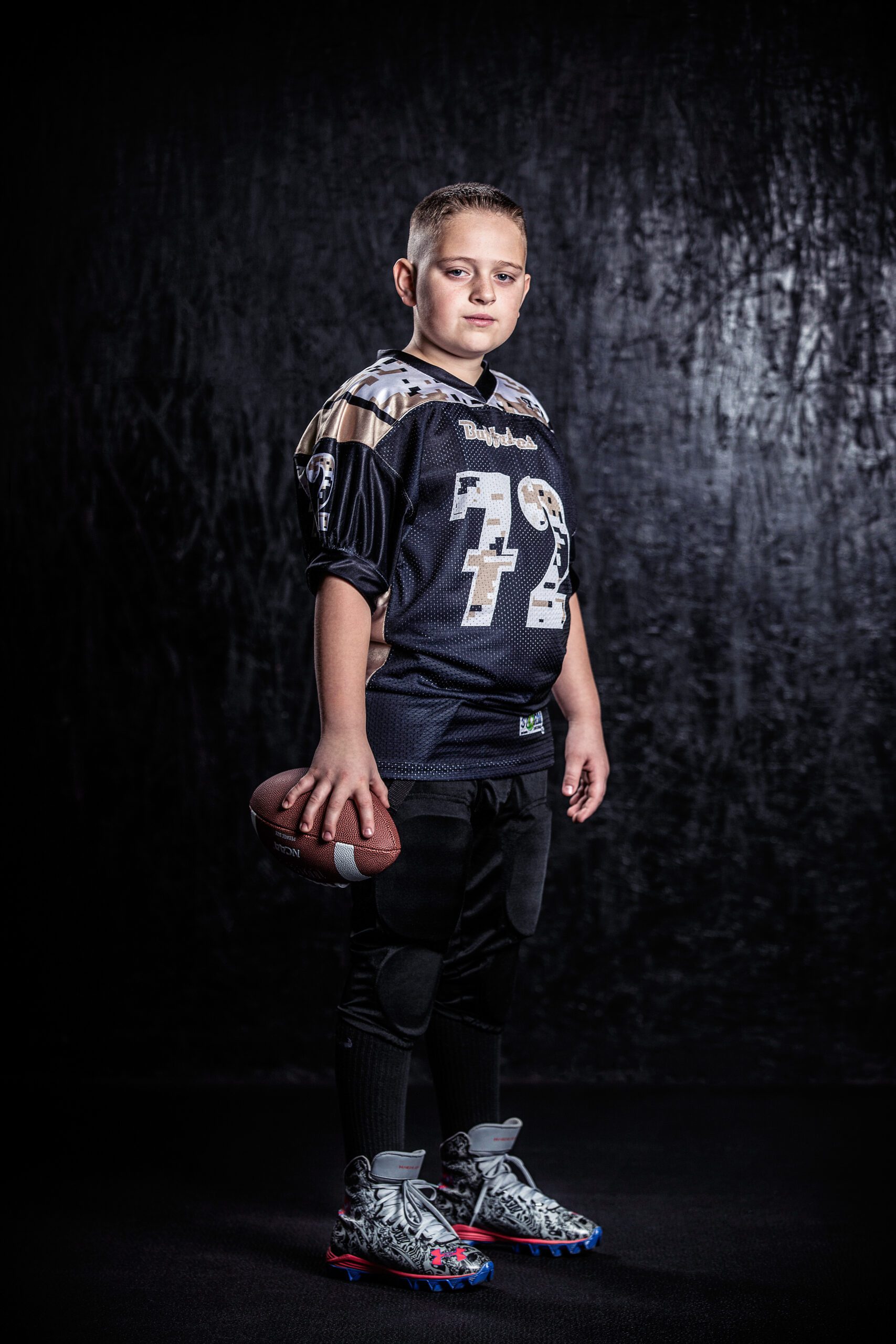 Young Athlete in Football Gear Holding a Ball Against a Dark Backdrop.
