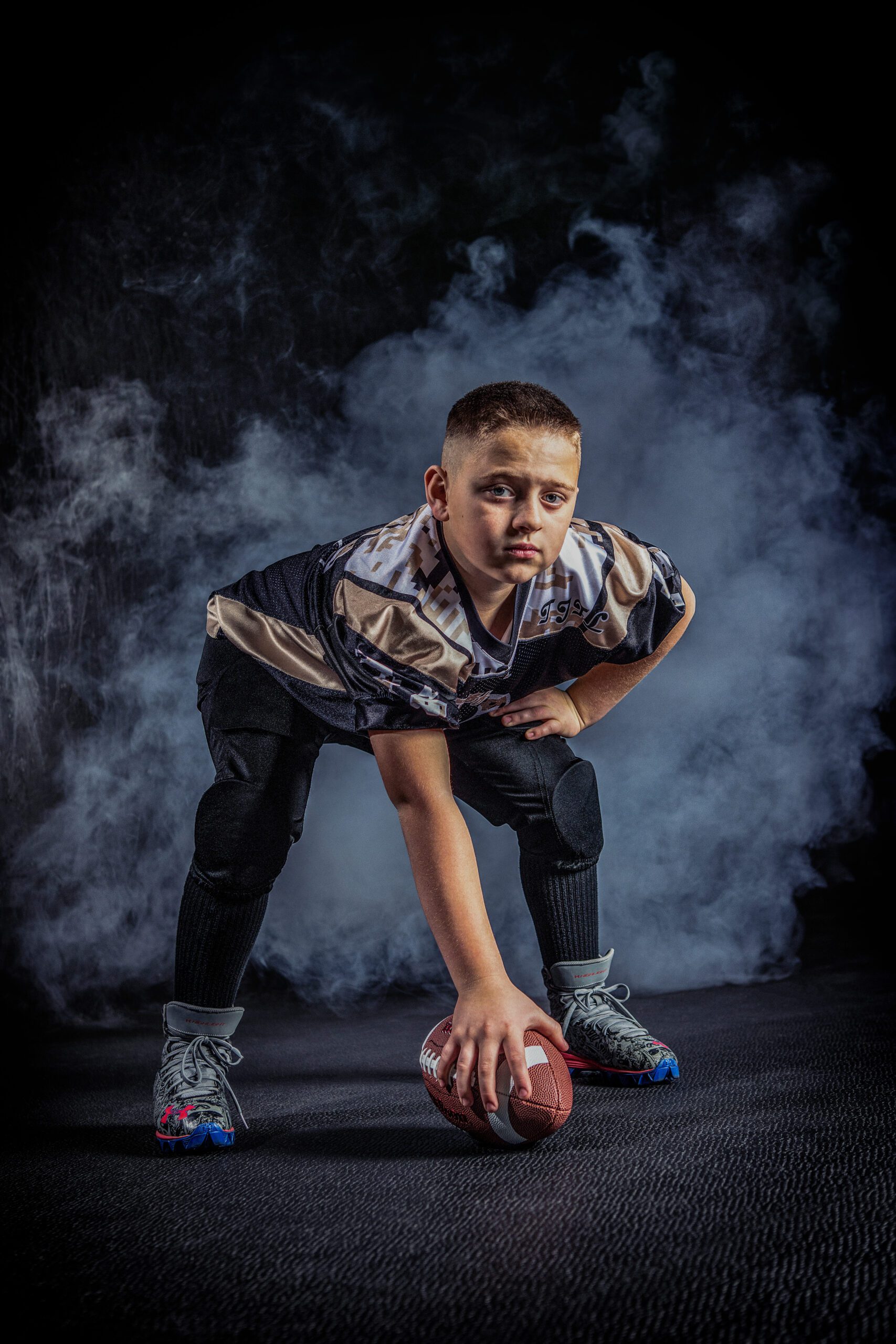 Young football player in a ready stance with a ball, surrounded by atmospheric smoke, conveying intensity and focus.