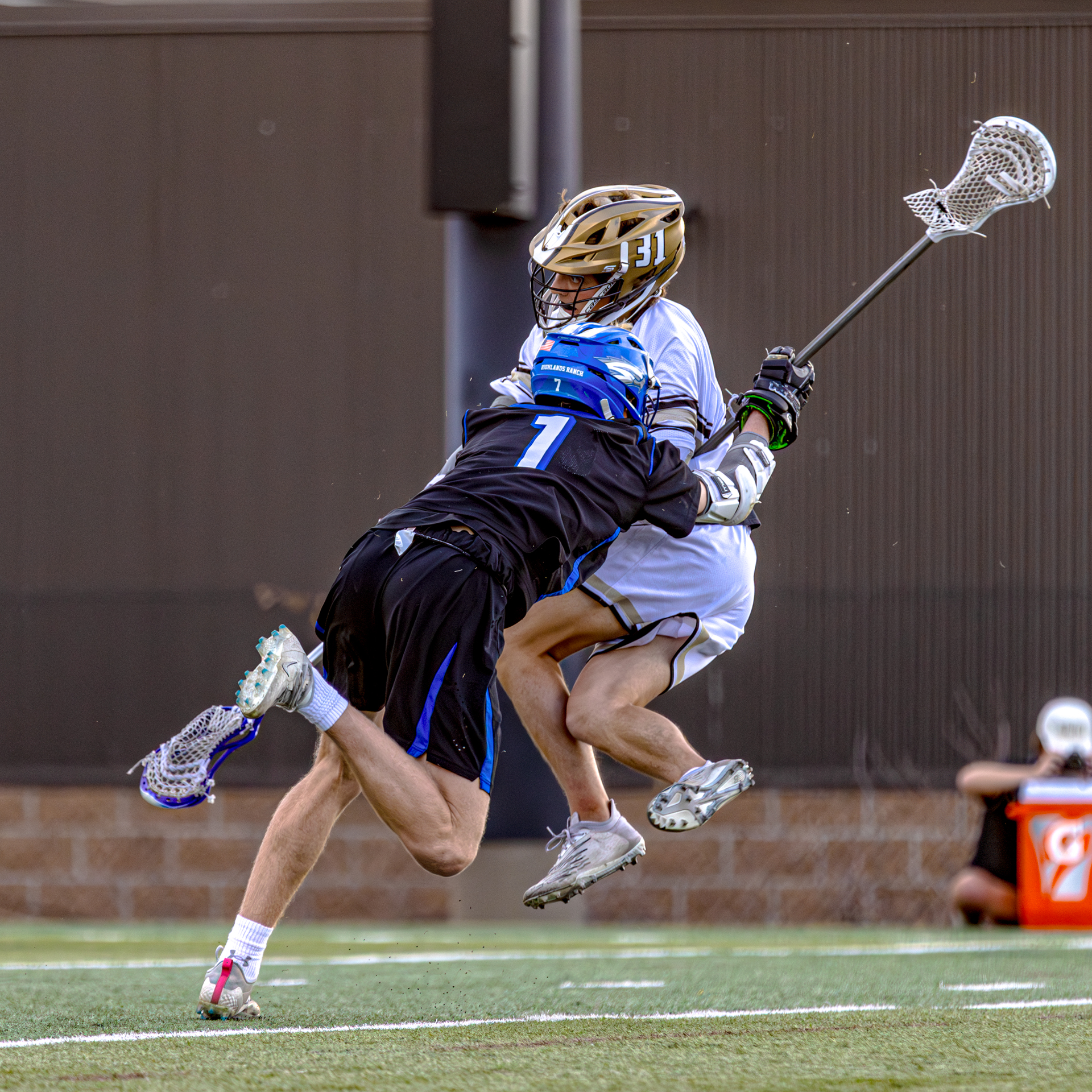 Highlands Ranch High School lacrosse defense player aggressively pushing aside an opposing team member during gameplay.